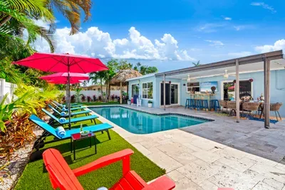 Private heated pool with lounge seating, covered outdoor dining and tiki hut at a Sunshine State Lux BNB Deerfield Beach vacation home