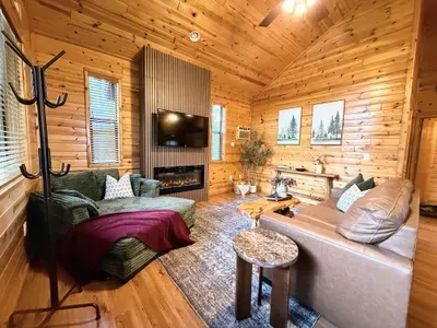 Cozy wood-lined cabin living room with fireplace, TV, and rustic charm