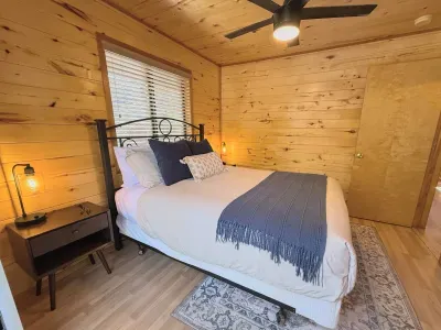 Cozy wood-paneled bedroom with queen bed, modern fan, and warm lamps