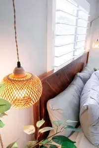 A serene, tropical-inspired bedroom designed for rest and relaxation. Warm woven pendant lighting, natural wood accents, crisp linens, and lush greenery create a cozy coastal atmosphere—perfect for unwinding after a day in the Florida sunshine.