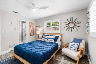Angler`s Alcove at Twin Oaks Coastal Luxury: a bright, coastal queen bedroom with nautical wall art, a roped sun mirror, Smart TV, and large plantation-shuttered windows letting in natural Florida light.