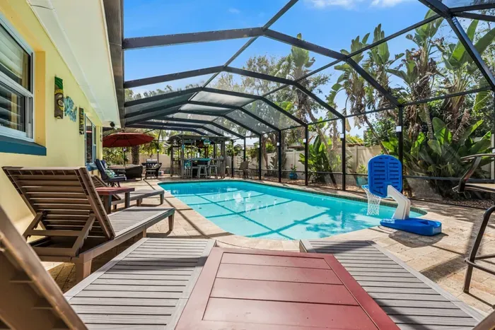 A sweeping view of the full screened backyard at Twin Oaks Coastal Luxury: the pool, Tiki Bar, lounge area, and lush tropical foliage — a complete private resort just minutes from Clearwater Beach.