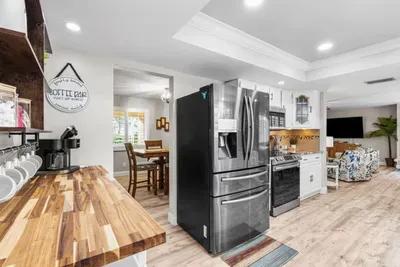 The dedicated coffee bar at Twin Oaks Coastal Luxury — a butcher block counter lined with mugs, a Keurig, and a 'Coffee Bar' sign — alongside stainless steel appliances including a French door refrigerator and gas range.