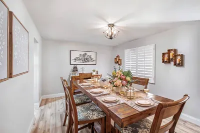 The elegant formal dining room at Twin Oaks Coastal Luxury seats six around a warm wood table with upholstered chairs, a matching sideboard, and soft nature-inspired art — ideal for a sit-down group dinner or celebration meal.