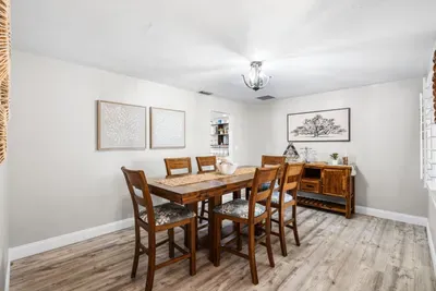 The elegant formal dining room at Twin Oaks Coastal Luxury seats six around a warm wood table with upholstered chairs, a matching sideboard, and soft nature-inspired art — ideal for a sit-down group dinner or celebration meal.