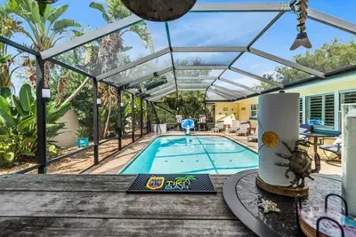 The view from the Tiki Bar bar top at Twin Oaks Coastal Luxury — looking out over the sparkling pool, sun loungers, and lush tropical banana trees inside the screened enclosure, with the Tiki Bar mat and coastal décor in the foreground.