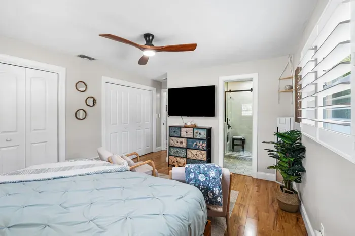 The primary Palm Paradise suite at Twin Oaks Coastal Luxury, showing the king bed, Smart TV, colorful painted dresser, and the open doorway into the private walk-in rain shower ensuite bathroom.