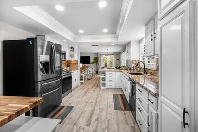 A wide-angle view of the fully equipped kitchen at Twin Oaks Coastal Luxury, featuring white shaker cabinets, granite countertops, stainless appliances including a French door refrigerator, and an open flow into the living areas.