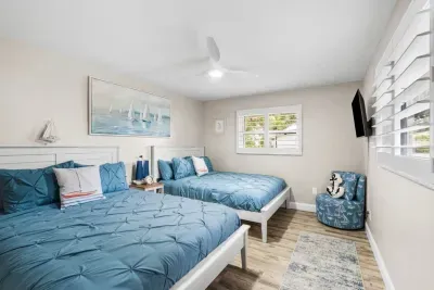 Sailor`s Cabin at Twin Oaks Coastal Luxury: two queen beds dressed in rich blue pinch-pleat bedding, a sailboat painting above the headboard, Smart TV, and a cozy anchor-print accent chair.