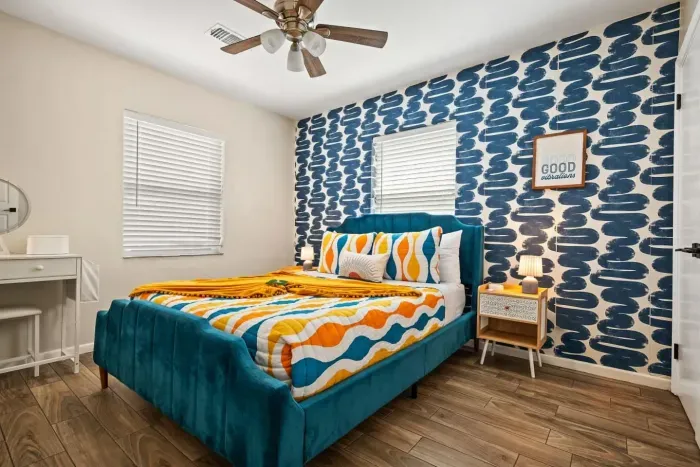 Queen bedroom with teal velvet bed, bold geometric wallpaper, and 'Good Vibrations' décor. St. Petersburg, FL vacation rental, sleeps 10.