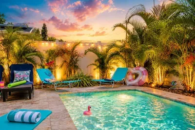 Private year-round pool surrounded by tropical landscaping, loungers, pool toys, and a fully fenced backyard—with heating included November through March.