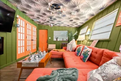 Disco Lounge alternate angle — coral sectional, orange French doors to backyard, TV wall, and retro accents throughout. St. Pete, FL.