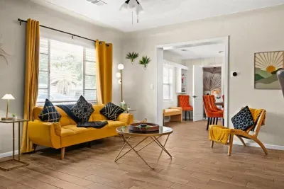 Bright living room — mustard yellow sofa, gold accent chair, natural light, open flow to dining room. 4-bedroom vacation rental, St. Pete, FL.