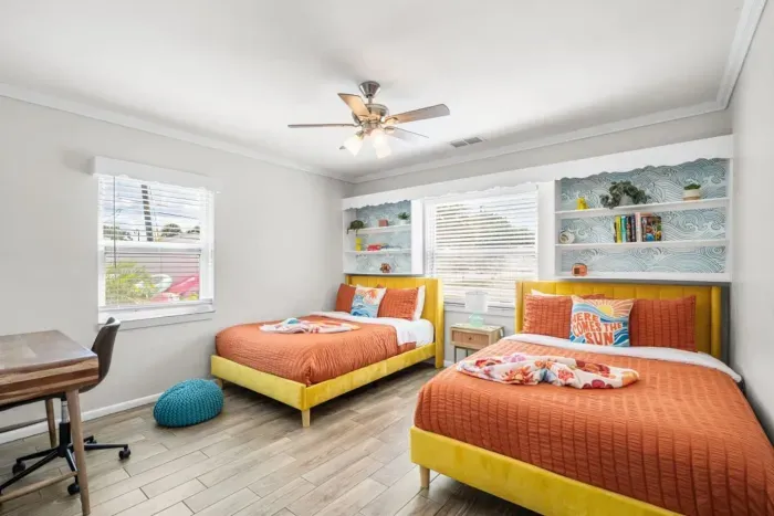 Two full beds with luxury bedding and yellow frames, ocean wave wallpaper, built-in shelving, and dedicated desk. 4-bedroom vacation rental, St. Petersburg, FL.