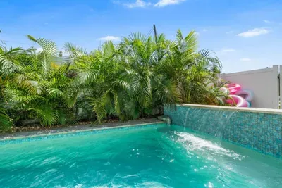 Pool waterfall feature — water cascades over teal mosaic tile into the private pool, surrounded by lush tropical palms. St. Petersburg, FL.
