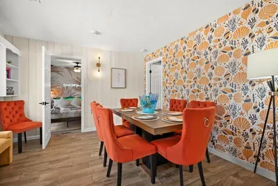 Dining room seats 6 — tufted burnt-orange velvet chairs, seashell accent wall, open sightline to primary suite. St. Petersburg, FL vacation rental.