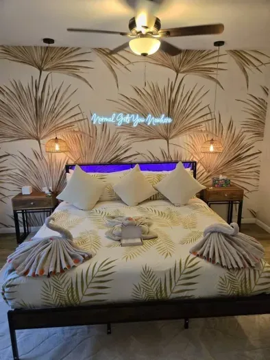 Primary king suite at night — glowing neon headboard, luxurious coastal bedding, and woven pendant lighting. Boutique-level finish in St. Petersburg, FL.
