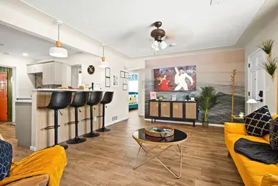 Open-plan living and kitchen — 65-inch smart TV, breakfast bar with 4 stools, and mustard yellow sofas. 4-bedroom vacation rental, St. Petersburg, FL.