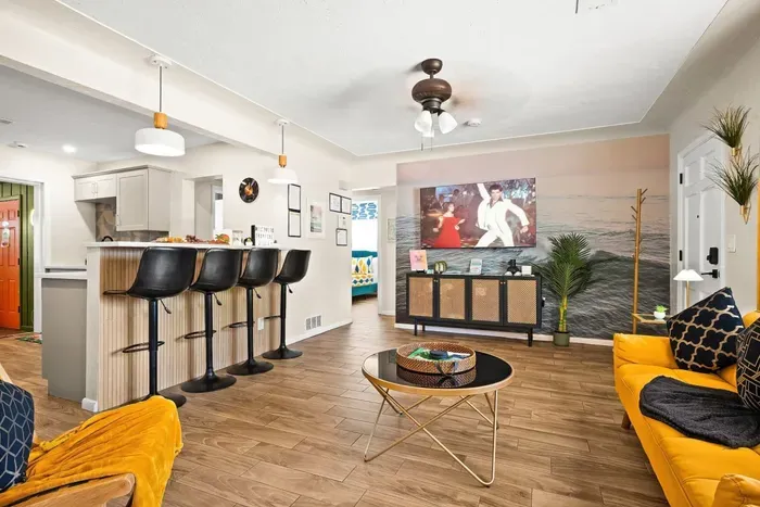 Open-plan living and kitchen — 65-inch smart TV, breakfast bar with 4 stools, and mustard yellow sofas. 4-bedroom vacation rental, St. Petersburg, FL.