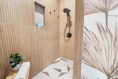 Walk-in rain shower in primary ensuite — wood-slat tile surround, dual rain and handheld showerhead, stocked toiletries niche. St. Pete, FL.
