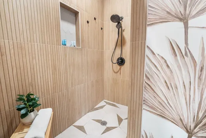 Walk-in rain shower in primary ensuite — wood-slat tile surround, dual rain and handheld showerhead, stocked toiletries niche. St. Pete, FL.
