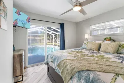 Primary bedroom — king bed with quality bedding, wall-mounted Smart TV, and direct sliding glass door access to the private screened pool.