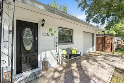 Welcoming front entry of Sun Oasis vacation rental in St. Petersburg, FL — stained glass door, sea turtle wall art, keypad smart lock, paver walkway, and a shaded porch bench set the tone before you even step inside.