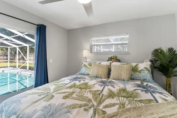Wake up steps from the pool — the primary bedroom with direct sliding door pool access, coastal luxury bedding, and soft natural light filtering through the screen enclosure.