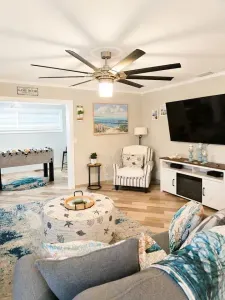 Coastal living room with comfortable seating, a fireplace credenza, a 65-inch Smart TV, an oversized starfish ottoman, and convenient access to the game room.