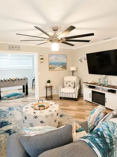 Coastal living room with comfortable seating, a fireplace credenza, a 65-inch Smart TV, an oversized starfish ottoman, and convenient access to the game room.