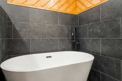 Spa-like soaking tub with sleek dark tile and warm wood ceiling