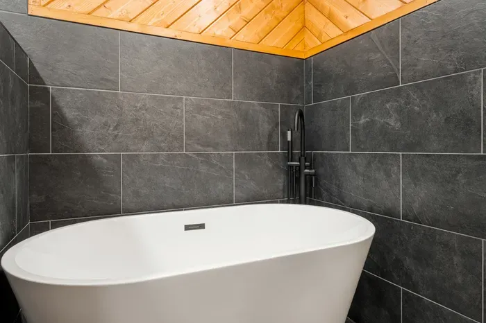 Spa-like soaking tub with sleek dark tile and warm wood ceiling
