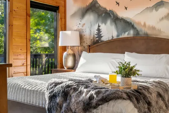 Cozy cabin-style bedroom with mural wall, plush bedding, and serene views