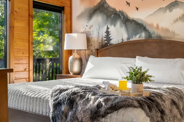 Cozy cabin-style bedroom with mural wall, plush bedding, and serene views