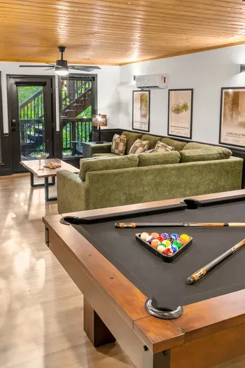 Cozy lounge with pool table, plush seating, and warm cabin-style charm