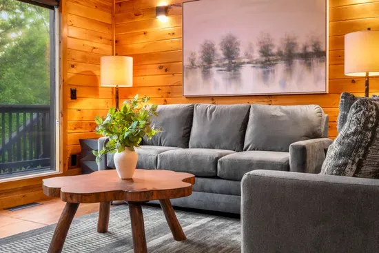 Cozy wood-paneled living room with plush seating and peaceful forest views