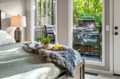 Sunny bedroom with private deck access, grill, and leafy outdoor views