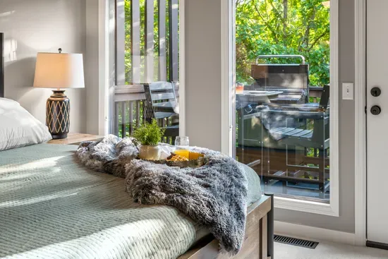 Sunny bedroom with private deck access, grill, and leafy outdoor views