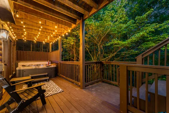 Private wooded deck with hot tub, string lights, and cozy lounge seating
