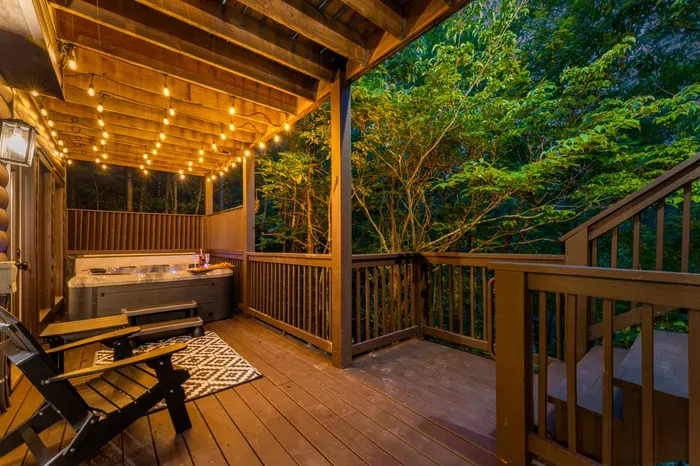 Private wooded deck with hot tub, string lights, and cozy lounge seating