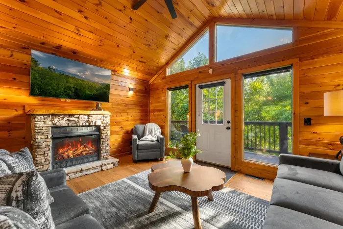 Cozy cabin living room with stone fireplace and sunlit forest views