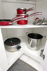 Well-stocked kitchen cabinet with pots, pans, and cooking essentials