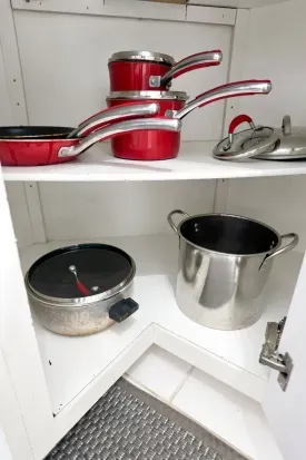 Well-stocked kitchen cabinet with pots, pans, and cooking essentials