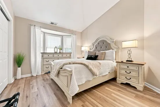 Bright, elegant bedroom with bay window, plush bedding, and warm natural light