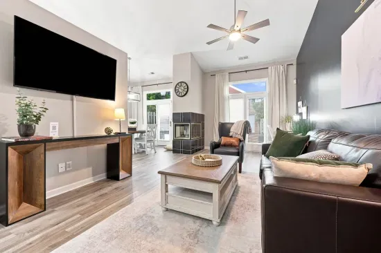 Bright open living room with fireplace, high ceilings, and large TV