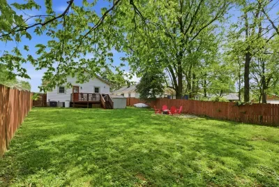 Spacious fenced backyard with deck, shade trees, and cozy fire pit area