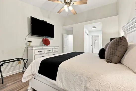 Bright, airy bedroom with king bed, TV, ceiling fan, and elegant decor