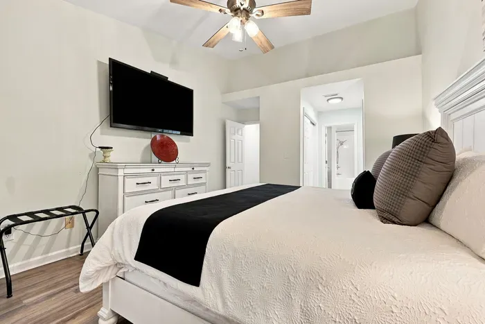 Bright, airy bedroom with king bed, TV, ceiling fan, and elegant decor