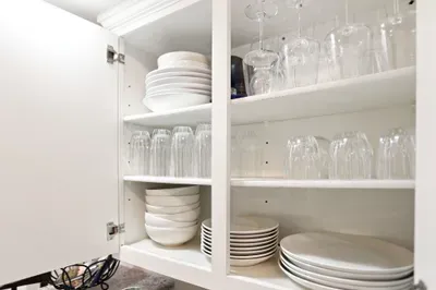 Well-stocked kitchen cabinet with organized dishes, glasses, and wineware