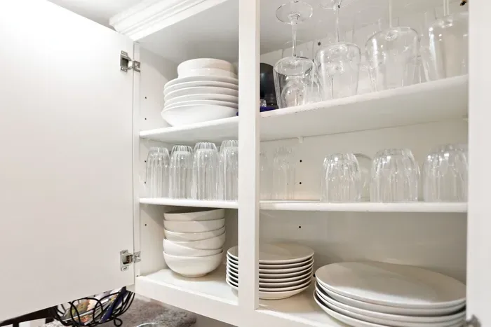 Well-stocked kitchen cabinet with organized dishes, glasses, and wineware